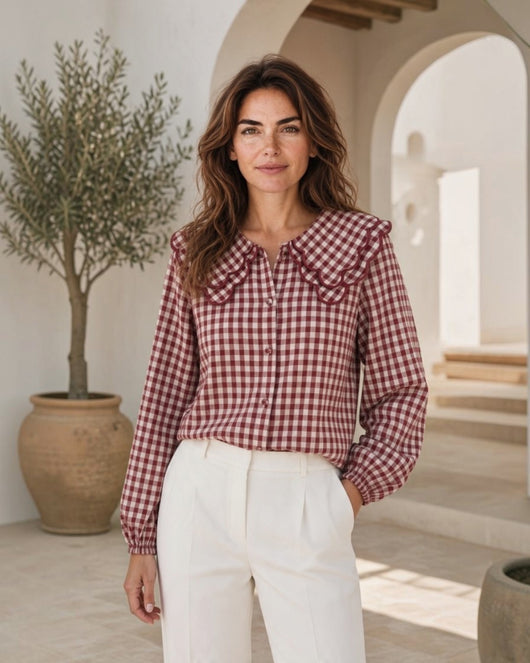 Blusa Maria Pailona com padrão vichy bordô e branco, gola de babados e mangas compridas, combinada com calças brancas.