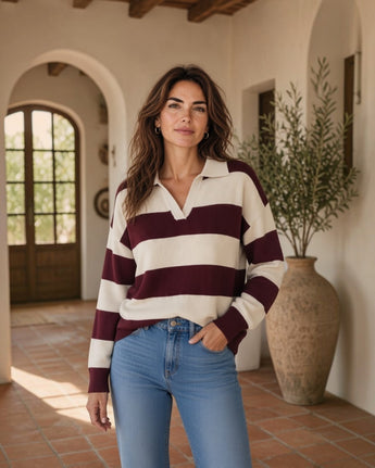 Mulher veste camisola de malha Maria Pailona com gola polo, riscas creme e bordeaux, combinada com calças de ganga.
