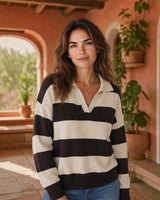 Mulher a usar camisola de malha Maria Pailona às riscas creme e castanhas com gola polo em ambiente exterior.