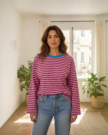Mulher a usar camisola Maria Pailona de manga comprida com riscas horizontais rosa e roxas e decote azul vibrante.