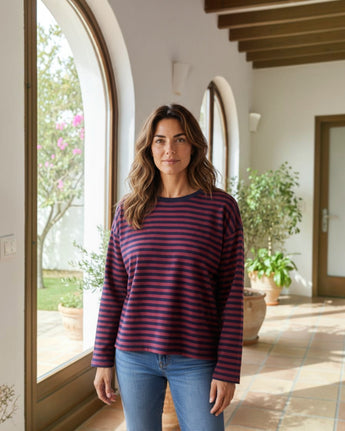 Mulher a usar camisola Maria Pailona de manga comprida com riscas horizontais bordeaux e azul-marinho e decote redondo.