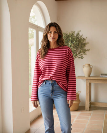 Mulher a usar camisola Maria Pailona de manga comprida com riscas horizontais em tons de rosa e vermelho e jeans