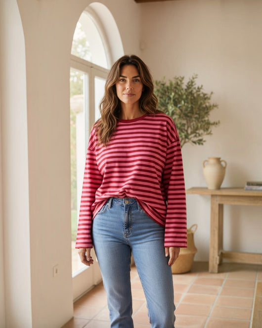 Mulher a usar camisola Maria Pailona de manga comprida com riscas horizontais em tons de rosa e vermelho e jeans