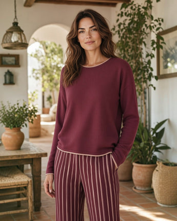 Conjunto de loungewear Maria Pailona com camisola bordô de decote redondo e calças às riscas verticais em ambiente casa